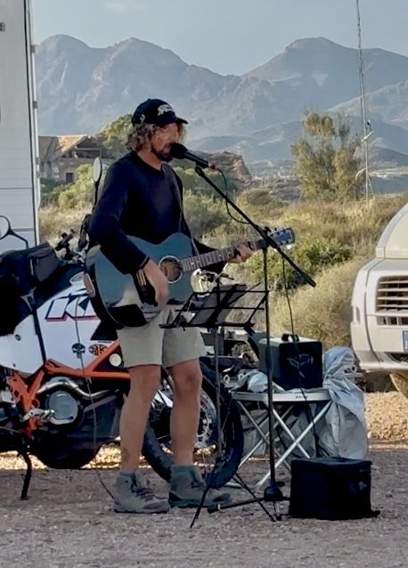 Pat playing guitar at a campsite, mountains in the background